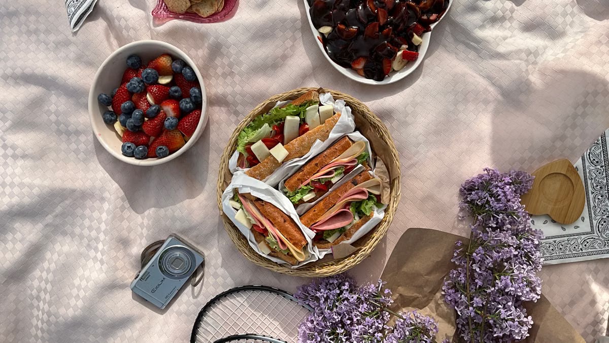 Enjoy a delicious picnic spread with sandwiches, fruits, and lilacs, captured in a top view style.